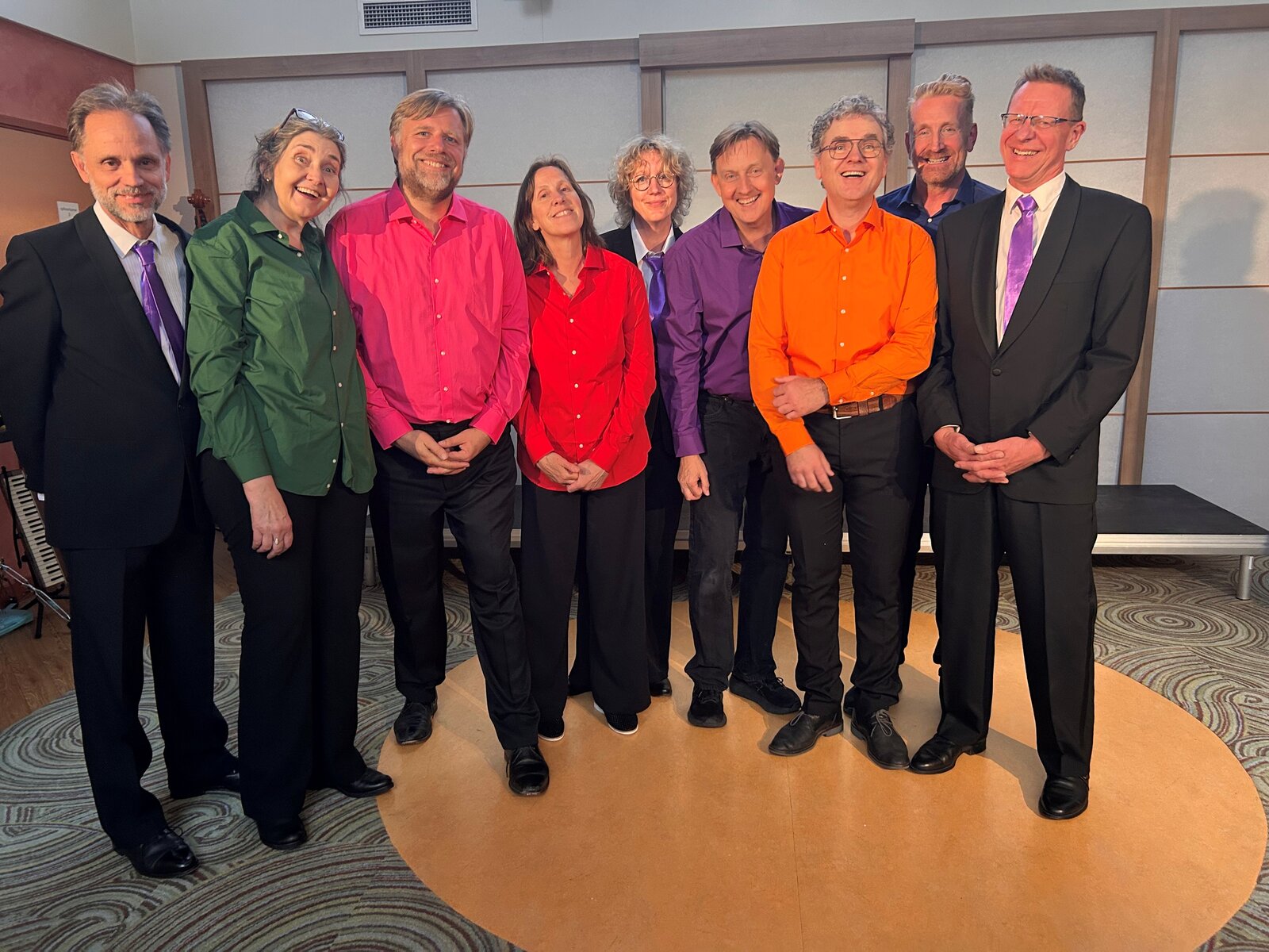 The nine members of Rauwe Vitrage smiling, in brightly coloured shirts and dark suits with purple ties