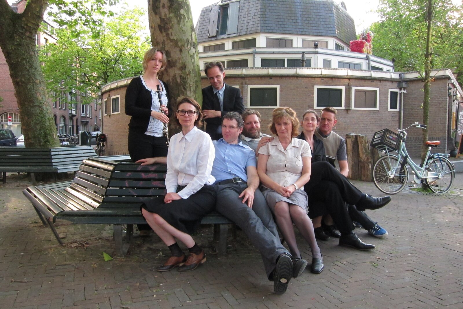 Rauwe Vitrage on a bench on Boerhaaveplein, with the round brick building of Mike's Badhuistheater behind them; one holds a clarinet